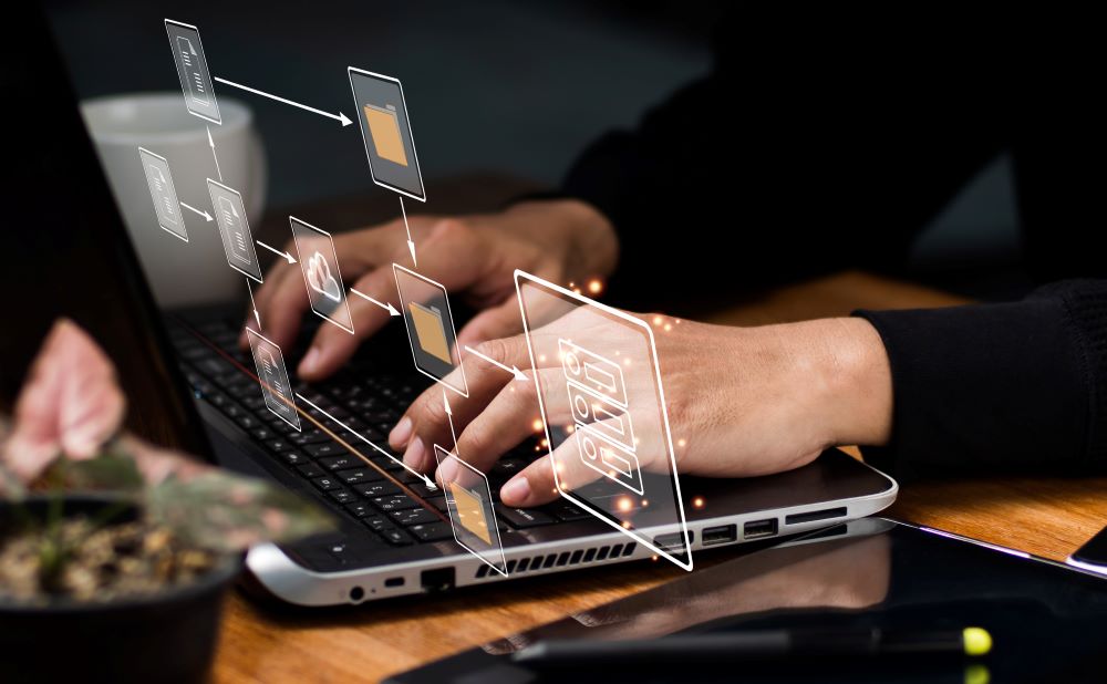 Close-up of hands typing on a laptop with digital icons symbolizing file and data transfer, representing backfile conversion services with a dynamic workflow in a dark office environment.