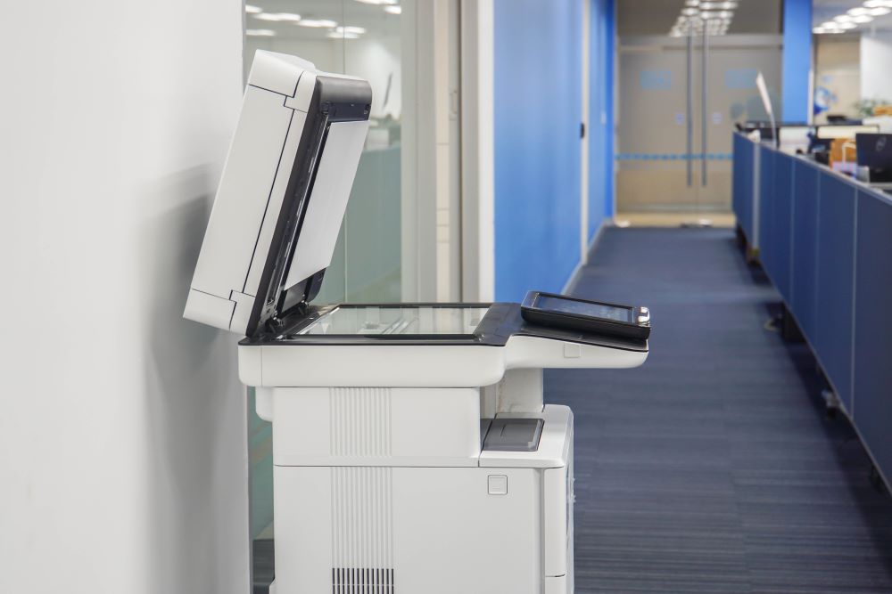 A modern color copier with an open document feeder positioned in a quiet office hallway, showcasing a potential setup for businesses considering a color copier lease.