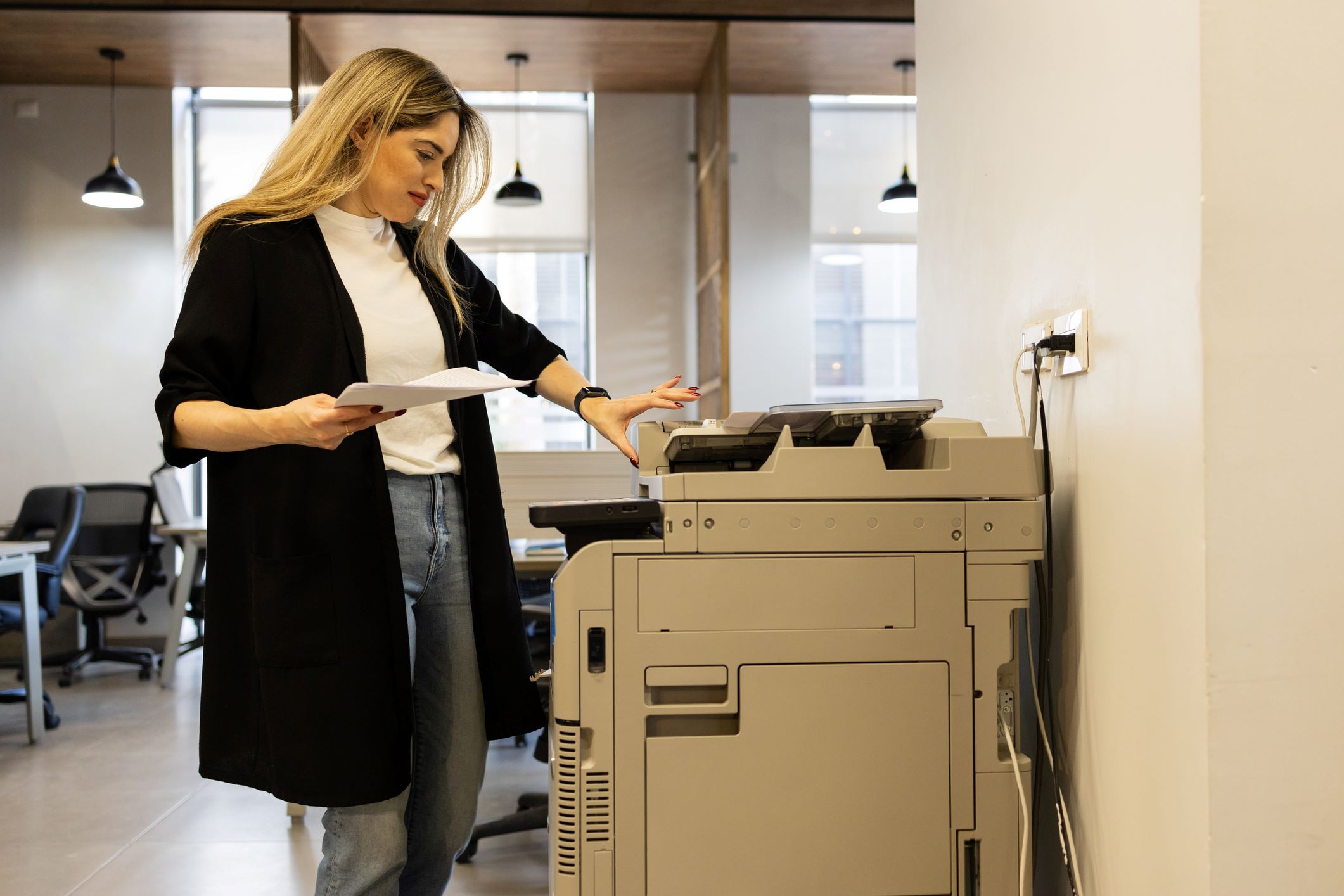 A woman in an office making copies with an office copier, illustrating the device's functionality and importance in everyday office operations.