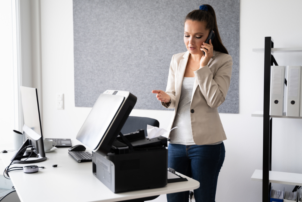 A businesswoman on the phone, troubleshooting a copier with an open lid, representing copier repair in an office setting.