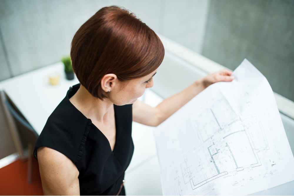 A woman reviewing architectural blueprints in an office, emphasizing the precision and clarity provided by a large format printer for detailed documents and designs.