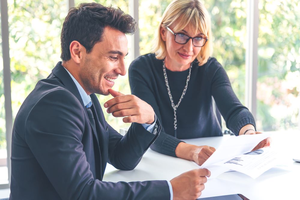 Two business professionals reviewing documents at a meeting, discussing copier rental options. The setting reflects a collaborative business environment focused on selecting cost-effective office solutions.