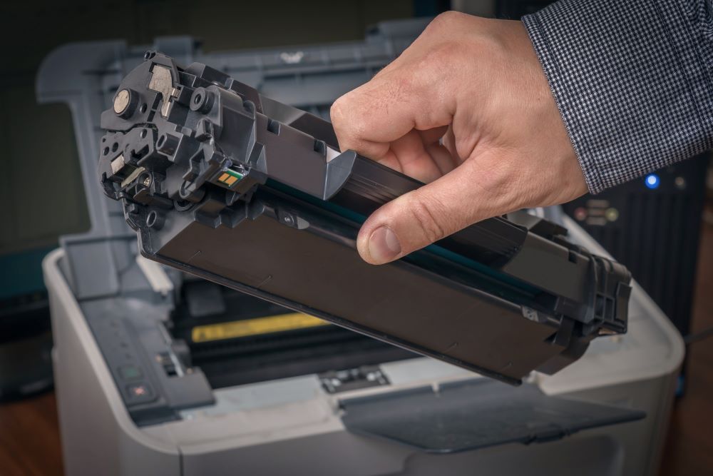 A technician performing copier service by replacing a toner cartridge in an office copier. Regular maintenance ensures optimal printer performance and longevity.