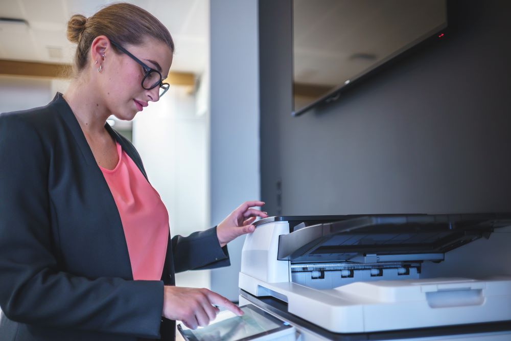 A businesswoman using an office copier to scan documents. Modern office copiers enhance productivity by providing printing, copying, and scanning solutions.