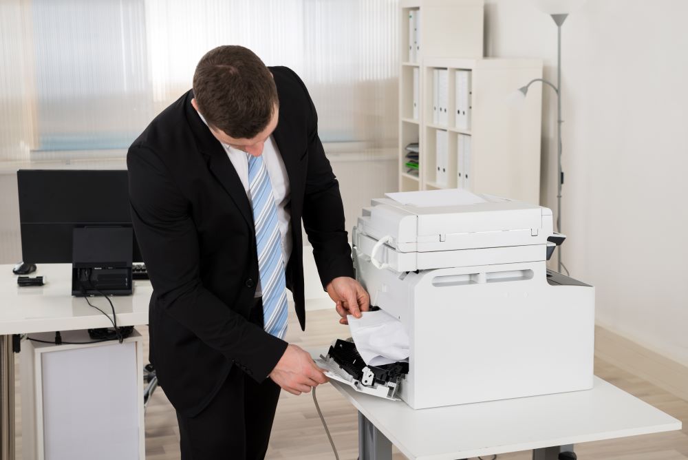 Office worker in a suit troubleshooting a paper jam in a copier, highlighting the importance of a reliable copier service provider for maintenance.