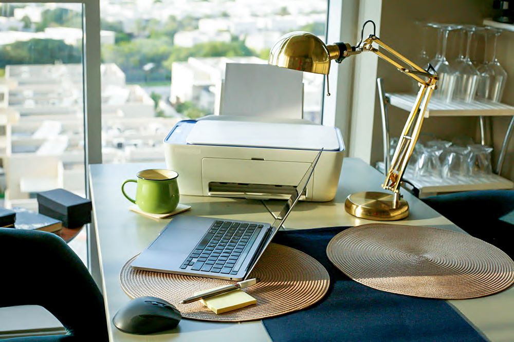 Office setup featuring an office printer, laptop, and desk lamp, showcasing a compact and efficient workspace for remote productivity.